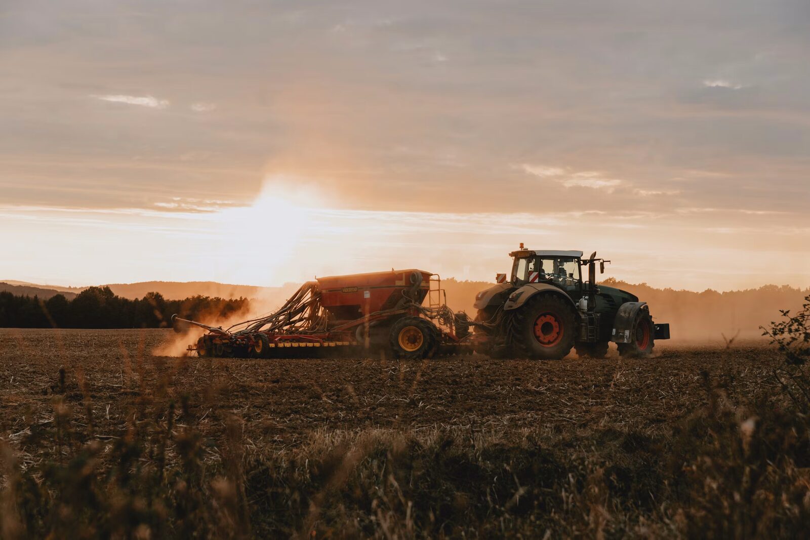 Tractor pulling implement through field at sunset