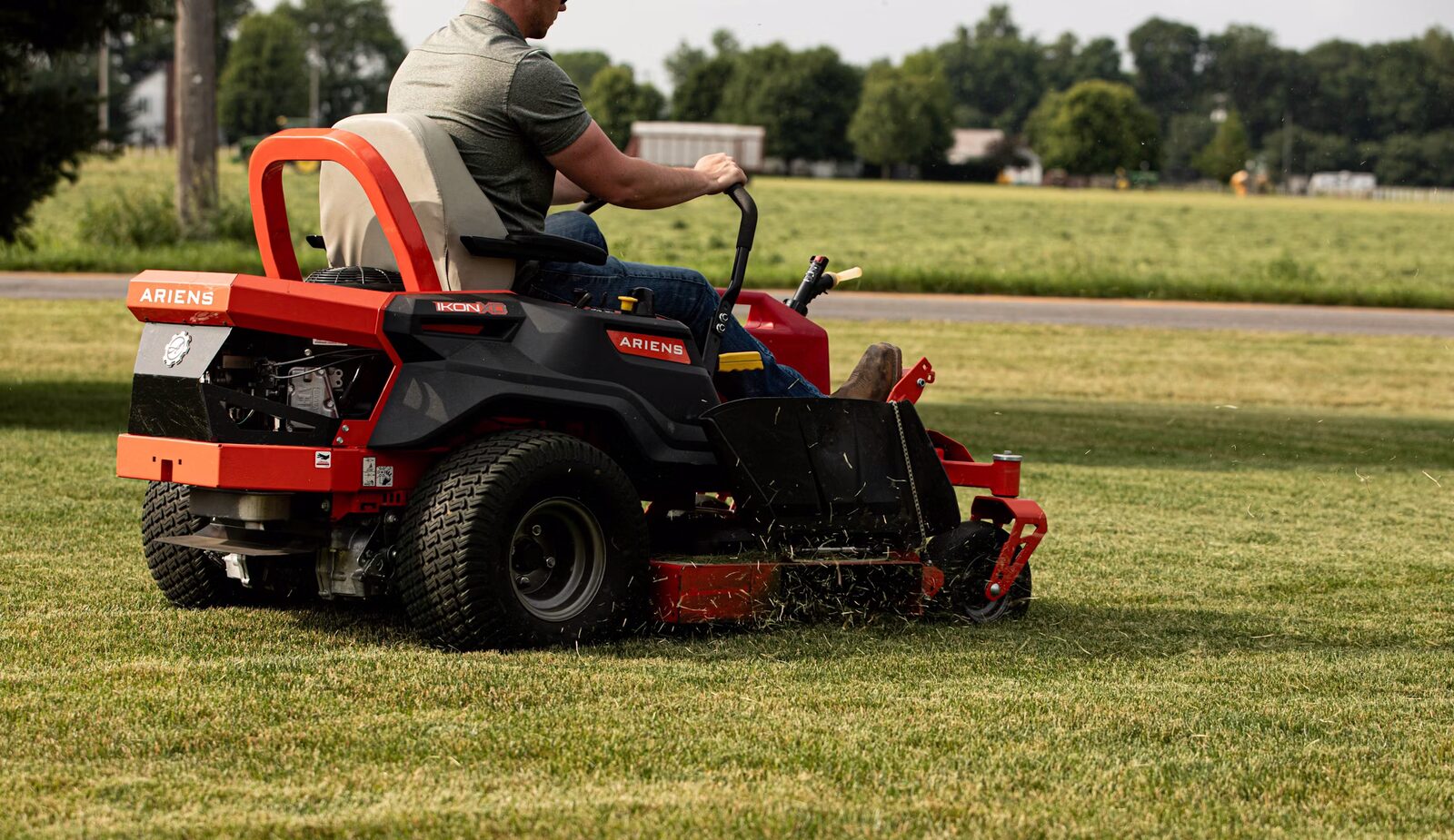 Rider mowing with clippings flying, rear three-quarter action
