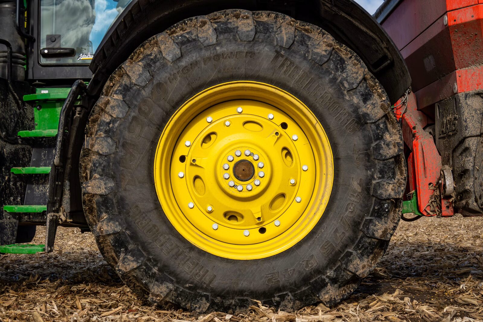 Mud-caked tractor lug tire with yellow rim, close-up